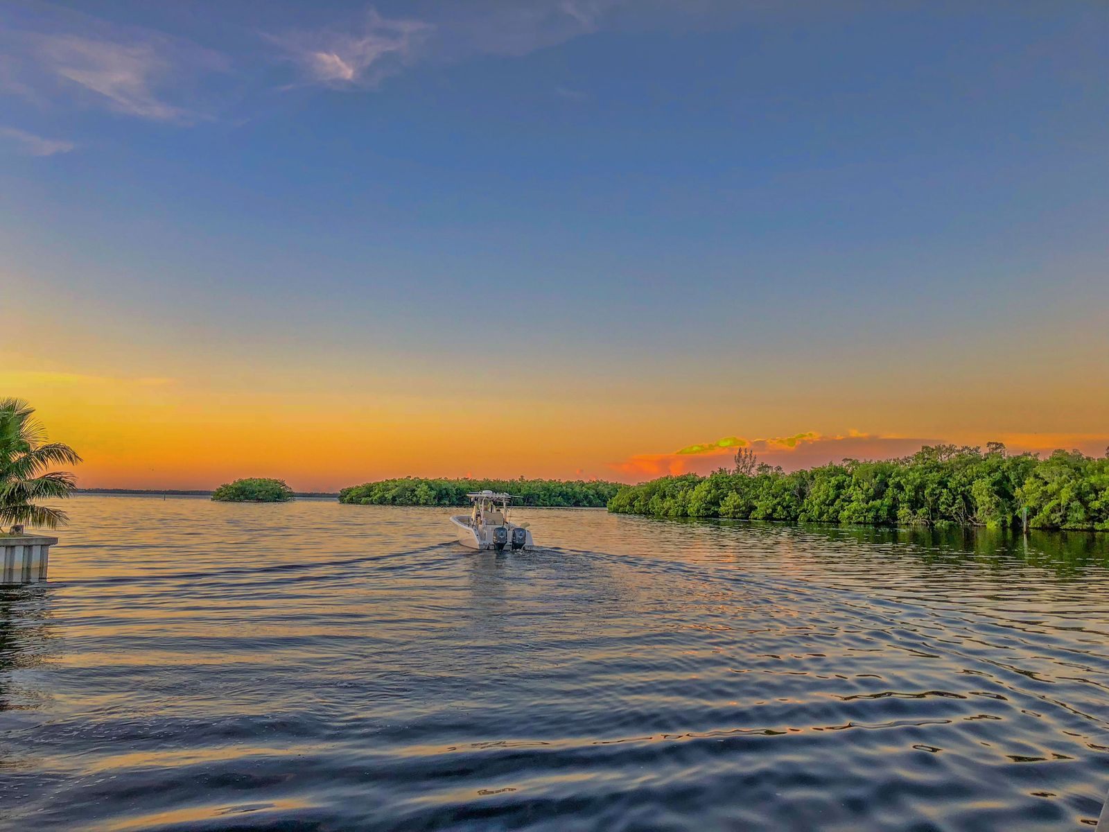 A small boat heading across calm water past mangroves at sunset in southwest Florida